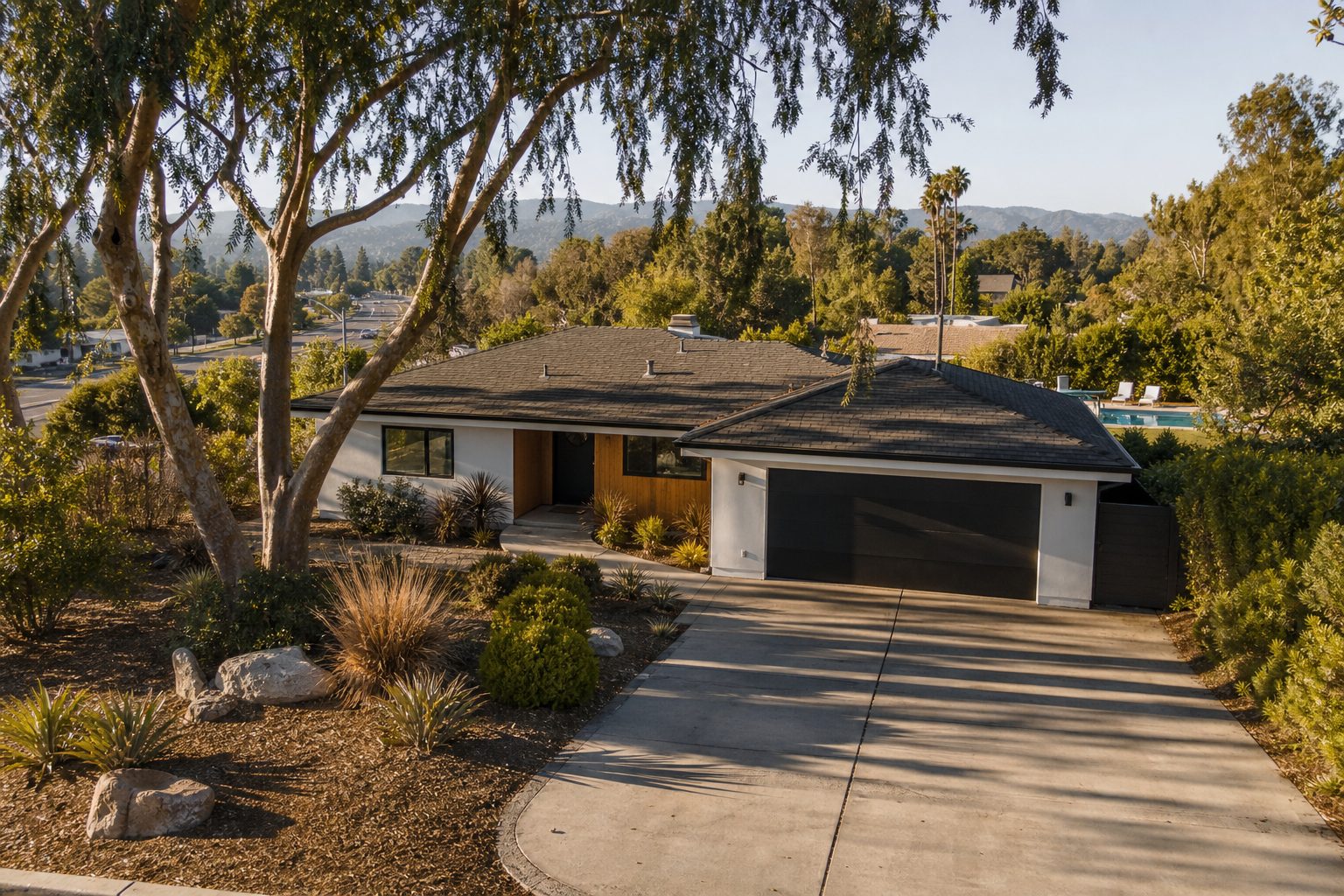 Single-story Woodland Hills ranch home with mature pepper trees, wide driveway, and pool visible in backyard at golden hour.
