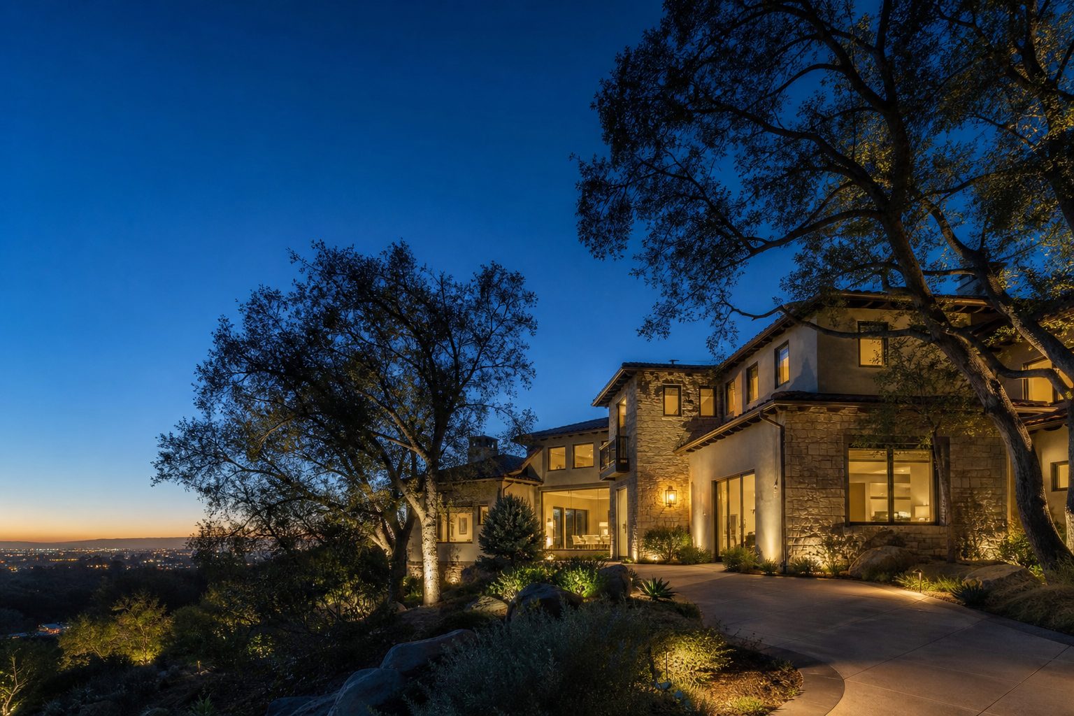 Contemporary Woodland Hills home with Mediterranean architecture and pool visible at twilight with interior window lighting and mature oak trees.