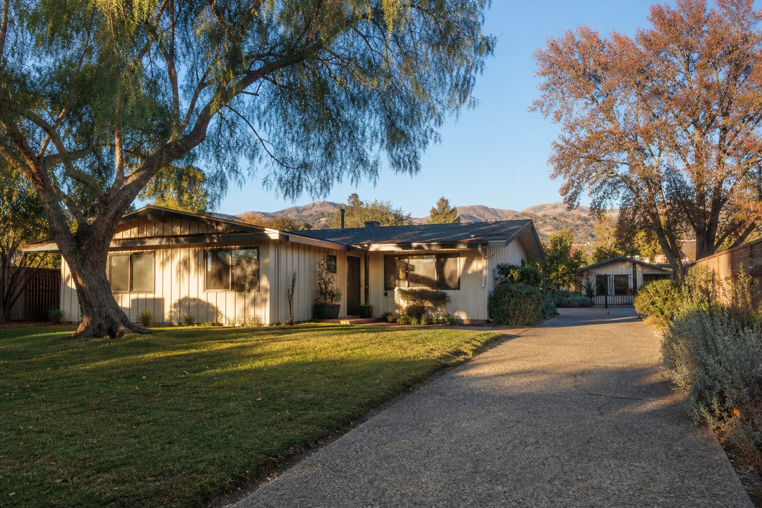 Detached ADU beside cream-colored mid-century home on spacious Northridge lot with mature trees and drought-tolerant landscaping.