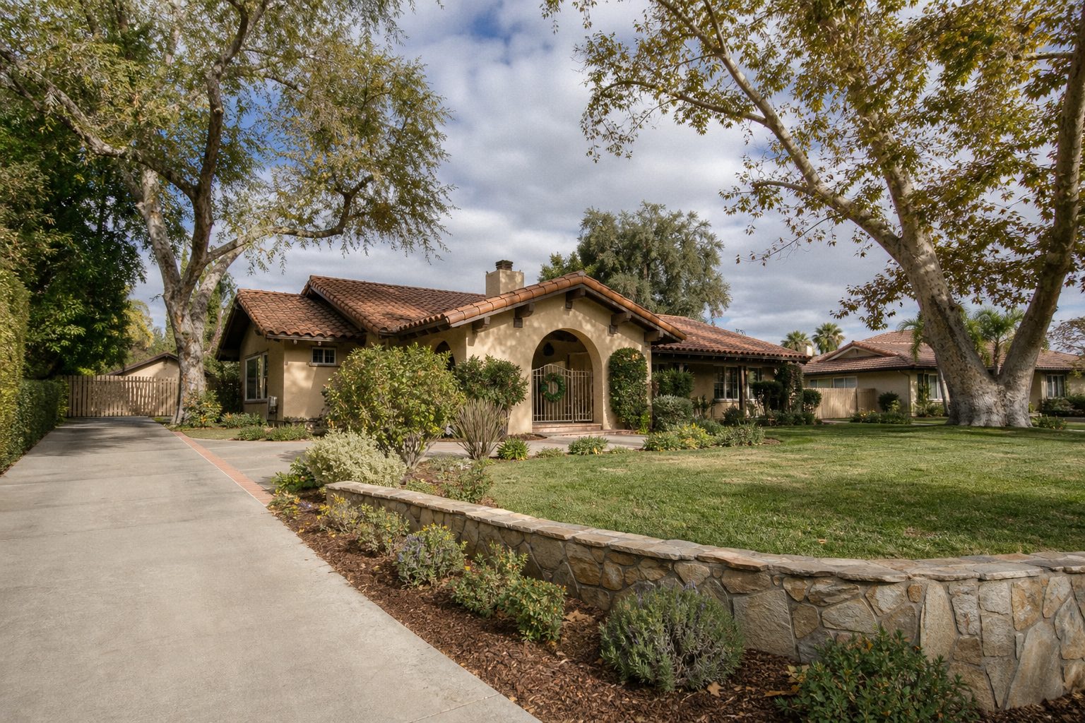Front-facing Northridge ranch home with mature trees and spacious lot, framed by natural landscape and adjacent homes in soft focus.