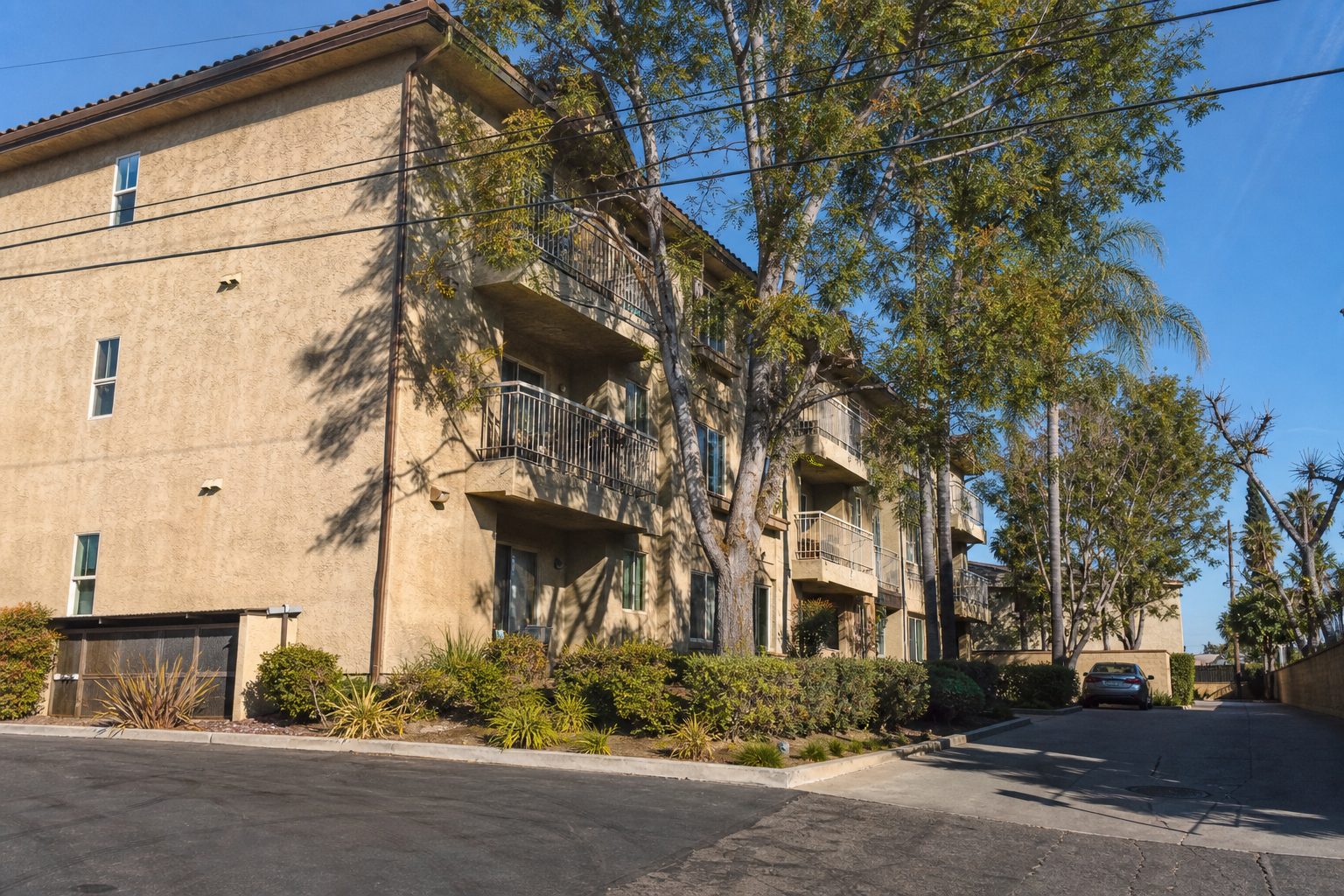 Three-story condo building in Northridge with mature trees, individual balconies, and authentic wear consistent with 1980s construction.