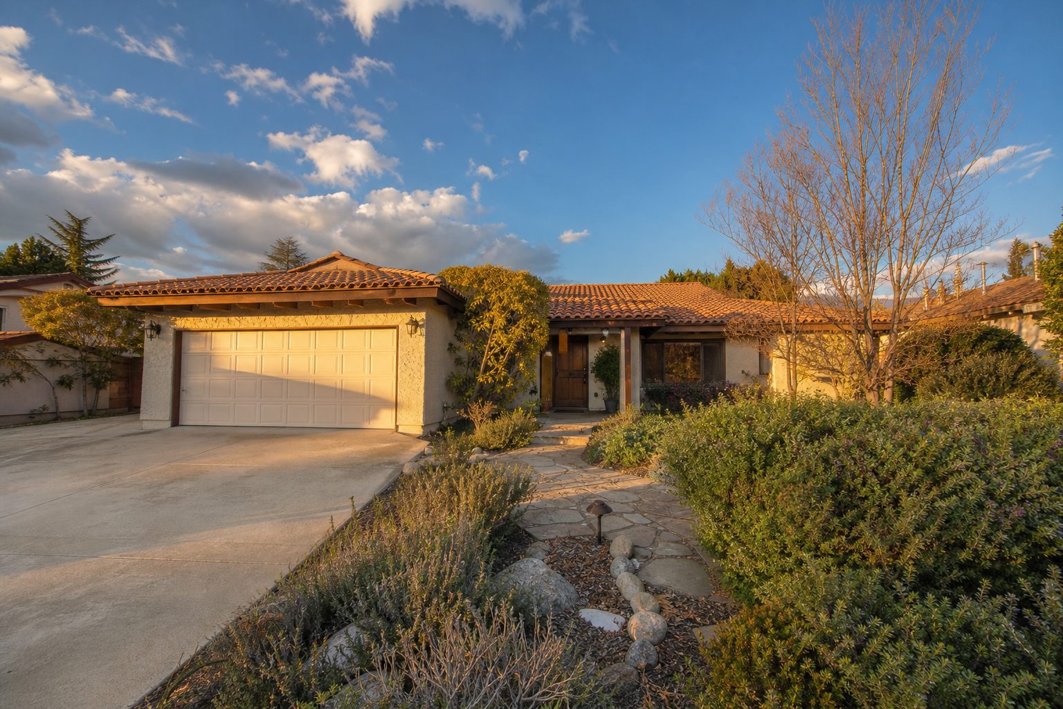 Single-family home with cream stucco and tile roof in Northridge with mature landscaping and wide driveway in afternoon sunlight.